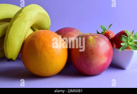 Un primo piano di vari frutti pieni di vitamine su sfondo viola Foto Stock
