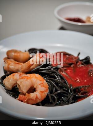 Un primo piano verticale di un delizioso gambero e spaghetti calamari su un piatto bianco Foto Stock