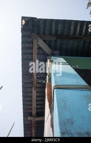 Una foto dal basso verso l'alto di un angolo di una casa di villaggio fatta di saccheggio di cemento. Il tetto della casa è fatto di lenzuola GCI. Foto Stock