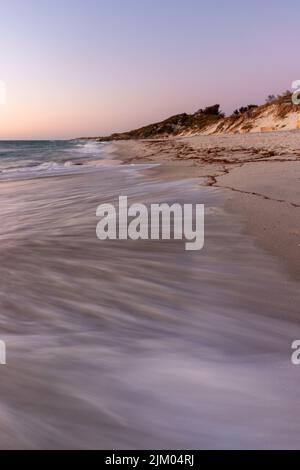 Una bella vista verticale delle onde che raggiungono la spiaggia sabbiosa sotto il colorato cielo del tramonto, girato in lunga esposizione Foto Stock