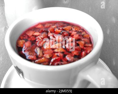 Tè rosso di frutta in tazza bianca con pezzi di frutta in esso. Foto Stock