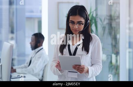 Trovare tutte le soluzioni intelligenti. Una giovane donna d'affari che indossa un auricolare e utilizza un tablet digitale in ufficio. Foto Stock
