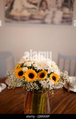 Foto verticale di fiori di margherita gialli e bianchi in un vaso di vetro su un tavolo di legno con teacup al coperto Foto Stock