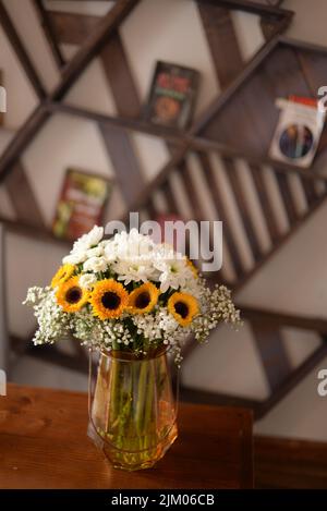 Un tiro verticale di un vaso decorativo con fiori bianchi e girasoli in un soggiorno Foto Stock