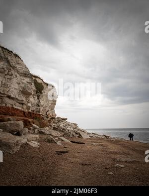 Coppia camminando lungo la spiaggia sotto le tempeste rainclouds alle vecchie scogliere di Hunstanton in Norfolk. Foto Stock