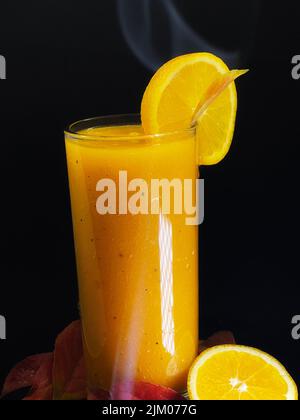 Un colpo verticale di succo d'arancia o di mango con una fetta d'arancia su sfondo scuro Foto Stock