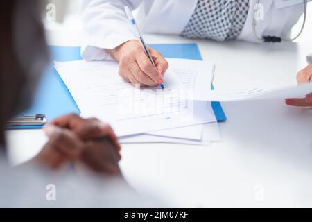 Questa paziente ha una grande assicurazione medica. Una dottore femminile che riempie i documenti del paziente alla sua scrivania. Foto Stock