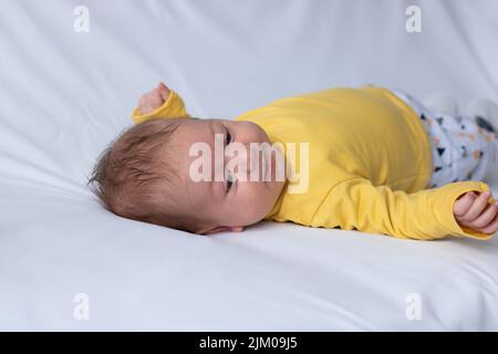 Un primo piano di un bambino caucasico, che indossa una camicia gialla, sdraiato su un tessuto bianco Foto Stock
