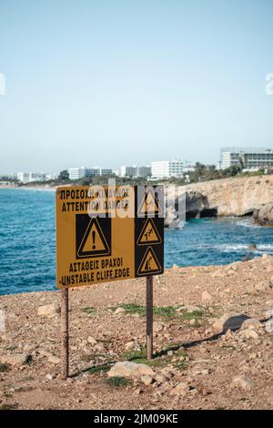 Segnale di precauzione sul bordo pericoloso vicino alle grotte marine in Ayia Napa, Cipro Foto Stock