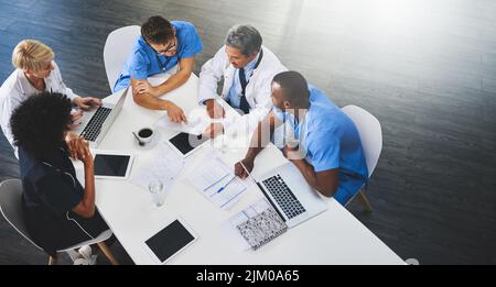 Team di medici che si siedono e si incontrano con i computer portatili intorno al tavolo. Medici e personale che discutono documenti e risultati dei test. Esperti sanitari Foto Stock