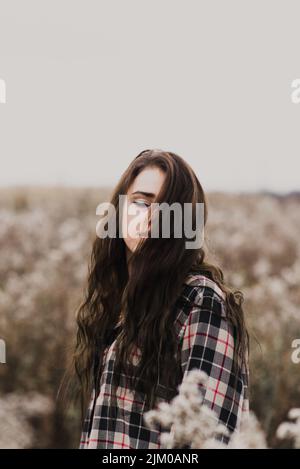 Un primo piano verticale di una ragazza in un campo in una camicia a quadri. Messa a fuoco superficiale. Foto Stock