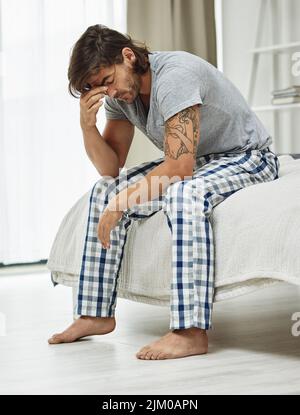 Non è così che volevo iniziare la mia giornata: Un giovane seduto sul letto che guardava depresso. Foto Stock
