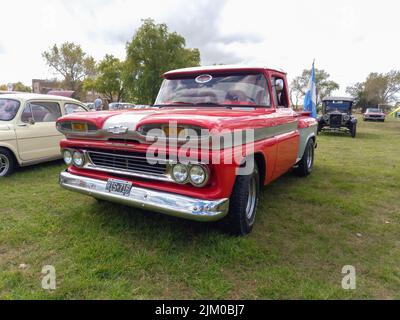 Chascomus, Argentina - Apr 09, 2022: Vecchio rosso Chevrolet Chevy C10 Apache pick truck 1960-1961. Verde erba sfondo natura. Strumento di utilità o di coltivazione Foto Stock