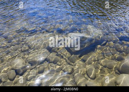 Un bel colpo di rocce e pietre sotto l'acqua con riflesso della luce del sole Foto Stock