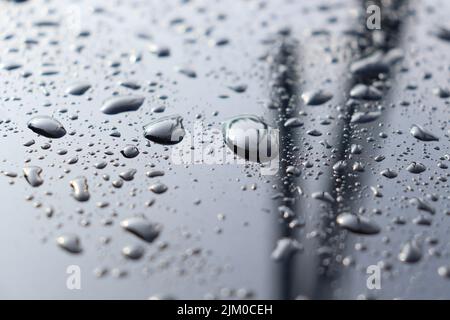 Fuoco selettivo di gocce d'acqua su una superficie riflettente nera Foto Stock