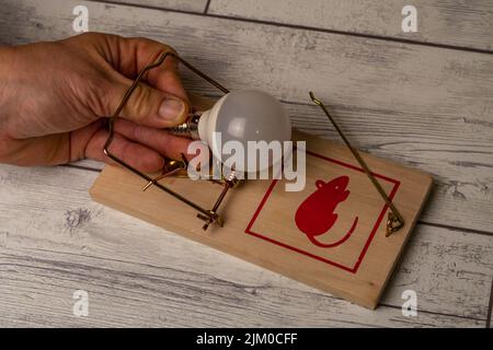 la mano di una donna viene catturata in un mousetrap mentre prende una lampadina, l'aumento dei prezzi dell'elettricità Foto Stock