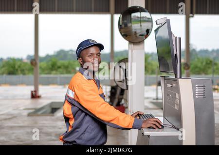 Un ingegnere maschio nero che utilizza una macchina indossando un'uniforme grigia e arancione Foto Stock