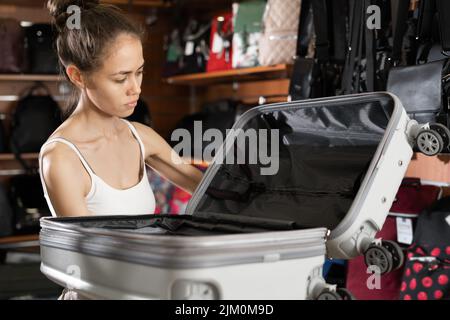 Giovane donna che sceglie una valigia da viaggio in un negozio. Donna acquirente in negozio Foto Stock