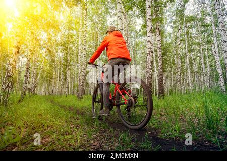 Donna in una giacca arancione brillante in bicicletta a cavallo sul sentiero della foresta in cima alla montagna Foto Stock