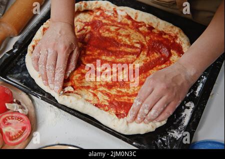 Vista dall'alto dello chef pizzaiolo che mette il formaggio feta sui lati dell'impasto mentre prepara gustosa pizza in cucina rustica. Foto Stock