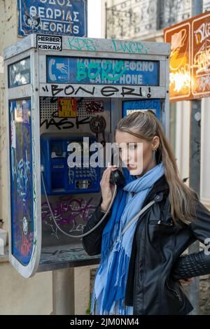 Un colpo verticale di una donna bionda caucasica che parla su un telefono a pagamento Foto Stock