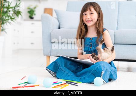 La ragazza disegna e gioca con un piccolo gattino, seduto sul pavimento a casa. Foto di alta qualità Foto Stock