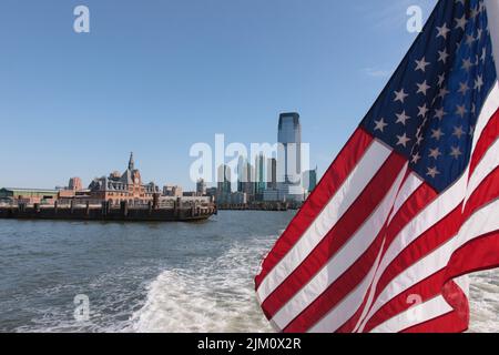 Primo piano di una bandiera americana sventolante contro una città sul mare Foto Stock