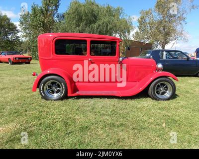 Chascomus, Argentina - Apr 9, 2022: Old Red Ford modello A Tudor Sedan 1928 - 1931. Asta di strada calda. Vista laterale. Natura verde erba e gli alberi sfondo. Foto Stock