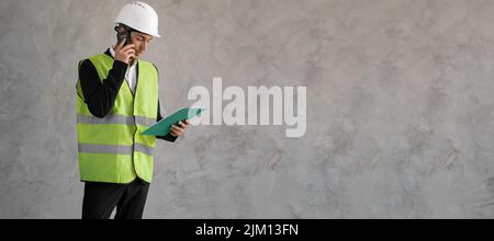 Responsabile del costruttore. L'ingegnere maschile parla al telefono. Progetti di carta di costruzione da architetto. Uomo in uniforme costruttore isolato su sfondo. Architetto Foto Stock