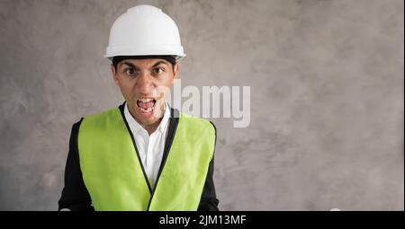 Giovane architetto musulmano uomo che indossa casco di sicurezza costruttore su sfondo isolato pazzo e pazzo urlando e urlando con emozione aggressiva Foto Stock