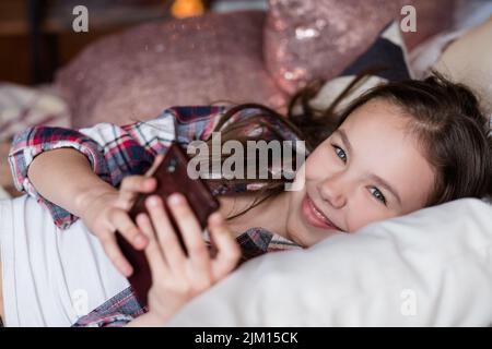 ragazza di piacere del bambino inattivo che usa il telefono cellulare a casa Foto Stock