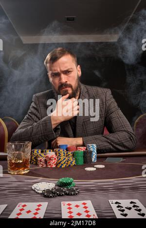 Bell'uomo barbuto sta giocando a poker seduto al tavolo nel casinò. Foto Stock