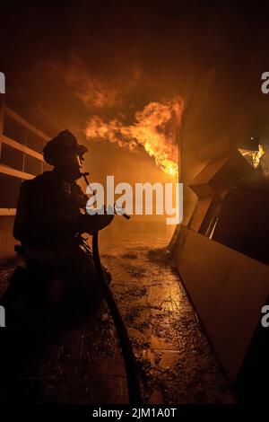 Un vigile del fuoco aspetta che il suo tubo venga caricato con acqua prima di attaccare il fuoco mentre i membri del Dipartimento del fuoco di Hampton Est sono stati Uniti da memb Foto Stock