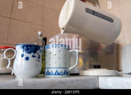 Una persona che versa l'acqua bollita alle tazze del tè. Consumo di energia, costo di vita concetto. Foto Stock