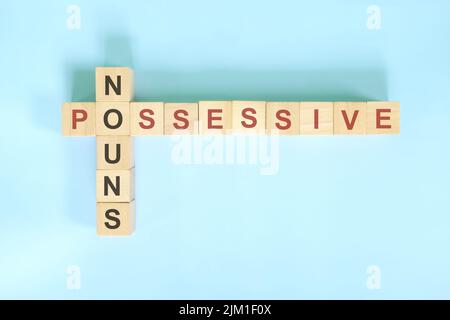 Concetto di sostantivi possessivi nell'educazione grammaticale inglese. Blocco di legno Crossword puzzle piatto adagiare su sfondo blu. Foto Stock