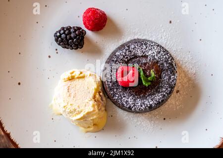 Fondente al cioccolato (cupcake) con lamponi, gelato e zucchero in polvere posto sul piatto Foto Stock