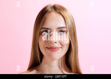 Primo piano volto di giovane bella ragazza, studente guardando la fotocamera isolato su sfondo rosa. Concetto di bellezza, arte, moda, emozioni umane Foto Stock