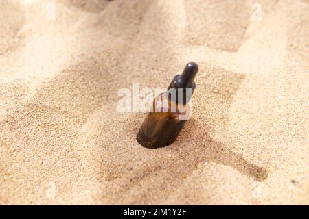 Siero cosmetico in un flacone di vetro con una pipetta nella sabbia Foto Stock