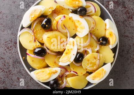 Insalata di patate con uova bollite, cipolle e olive condite con salsa di senape da vicino in un piatto sul tavolo. Vista dall'alto orizzontale dall'alto Foto Stock