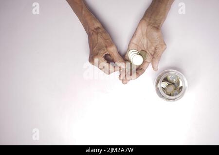 vista dall'alto delle monete a risparmio di mano delle donne anziane in un vaso Foto Stock
