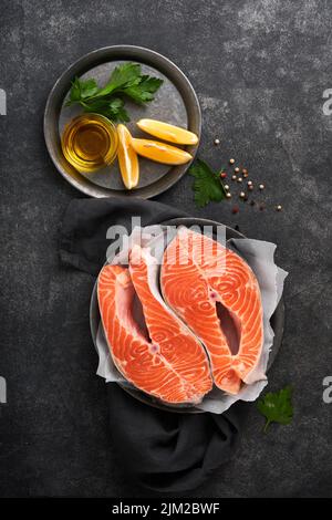 Salmone. Bistecca di salmone crudo. Pesce fresco di salmone crudo con ingredienti di cottura, erbe e limone preparato per cottura alla griglia su sfondo nero. Foo sano Foto Stock