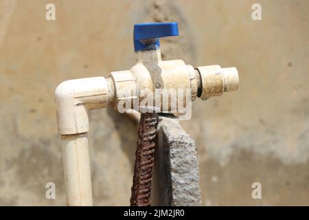 Rubinetto d'acqua o rubinetto fatto da materiali quasi riciclati poggiando su una pietra sostenuta da ferro arrugginito barra su un piccolo villaggio Foto Stock