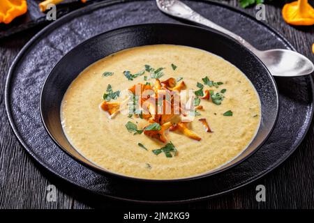 Kanttarellikitto, zuppa finlandese di Chanterelle in ciotola nera su tavola di legno scuro con cucchiaio, vista orizzontale dall'alto, primo piano Foto Stock