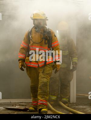 Vigile del fuoco che esce da un edificio in fiamme Foto Stock