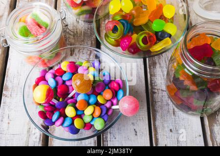 Vista ad angolo alto di vari lecca e caramelle multicolore in ciotole e vasetti su un tavolo di legno Foto Stock