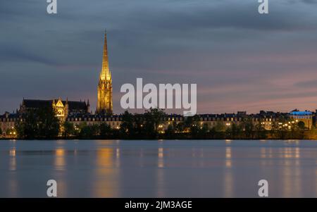 Skyline di Bordeaux al tramonto con la Basilique Saint-Michel e la Porte de Bourgogne illuminata e il fiume Garonna in primo piano Foto Stock