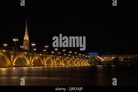 Pont de Pierre che attraversa il fiume Garonna nella città di Bordeaux illuminata di notte con la Basilique Saint-Michel sullo sfondo Foto Stock