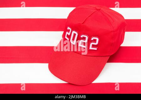 Cappello rosso TIPO MAGA con data 2022 sulla bandiera delle stelle e delle strisce degli Stati Uniti. Per le vittorie repubblicane in 2022 elezioni di Midterm degli Stati Uniti in novembre & Red Wave repubblicano degli Stati Uniti Foto Stock