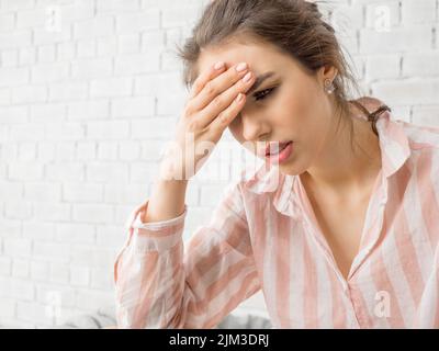 Foto da vicino di una donna con grave mal di testa. Tiene la fronte e cerca di affrontare il dolore. Foto Stock