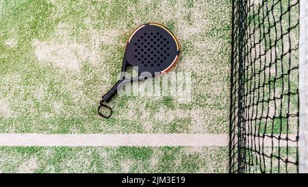 Vista dall'alto di un racket di padel nero su un prato verde dietro la rete all'aperto. Paddle è un gioco di racquetball. Concetto sportivo professionale con spazio Foto Stock